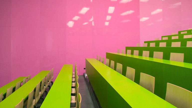 A lecture hall with pink colored walls and bright green seats