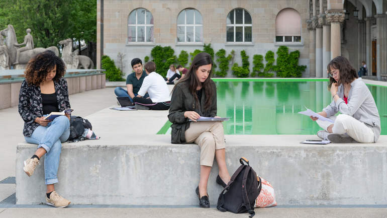 Three students are sitting next to the pool at the U Z H main building 